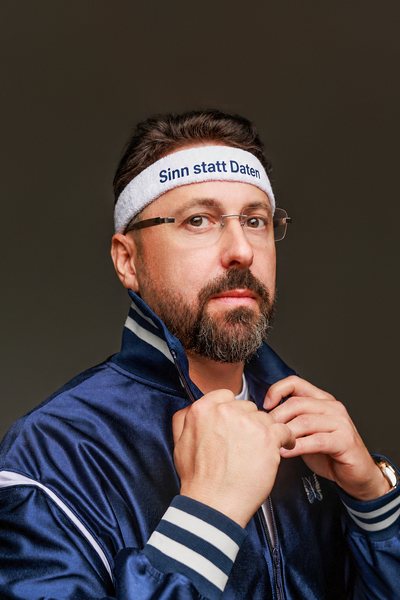Niko Martzy in blauer Trainingsjacke mit Stirnband „Sinn statt Daten“, das Motiv des Buchcovers